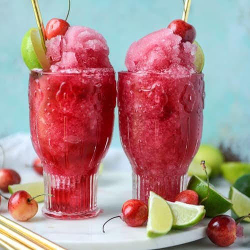 Cherry wine slushies served in glasses with fresh cherries and lime wedges.